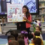 Unicorn Jazz book presentation in a library with children listening to a woman holding a plush unicorn toy.
